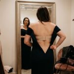 Woman wearing an off-the-shoulder evening dress checking strapless bra support in front of a boutique mirror